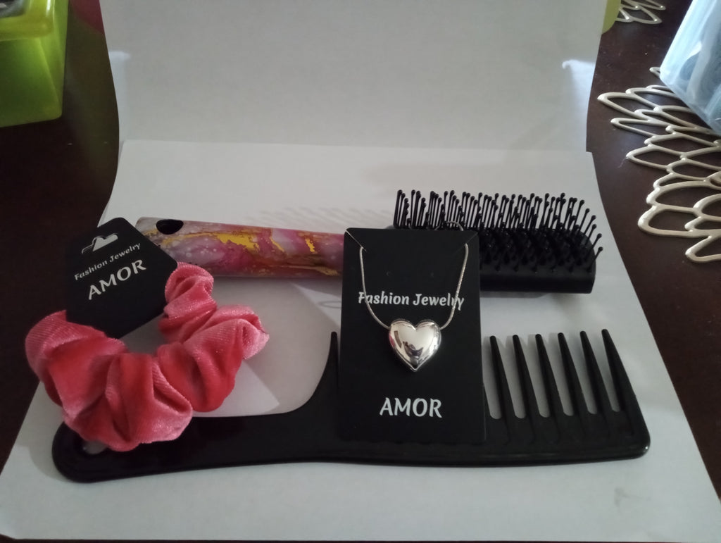Pink scrunchie, heart-shaped necklace, and black comb on a white surface with 'AMOR' branding.